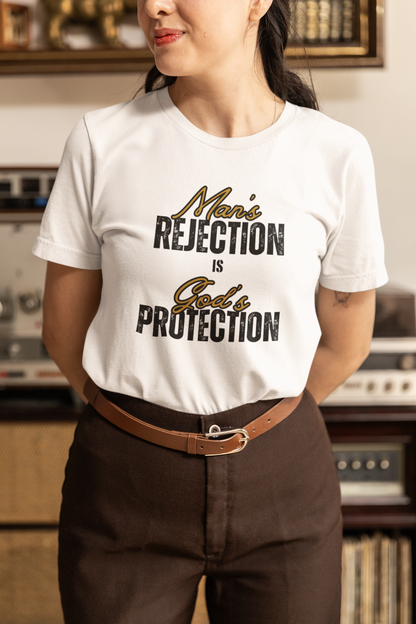 Christian wearing a white t-shirt with text that reads Mans Rejection is Gods Protection.