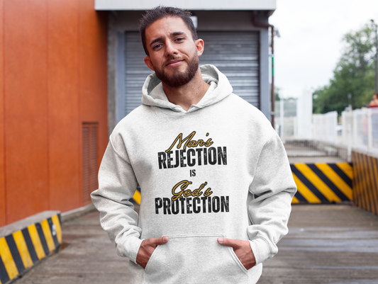 Christian Hoodie. Man wearing a white hoodie with  with text that reads  Man's Rejection is Gods Protection on  the front of the Hoodie, standing outdoors near a building.